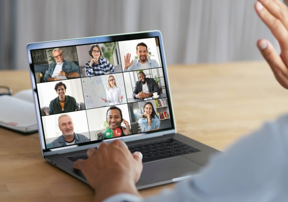 Online meeting, group brainstorming concept. Successful man waving his hand at the laptop computer screen, greeting employees during an video conference